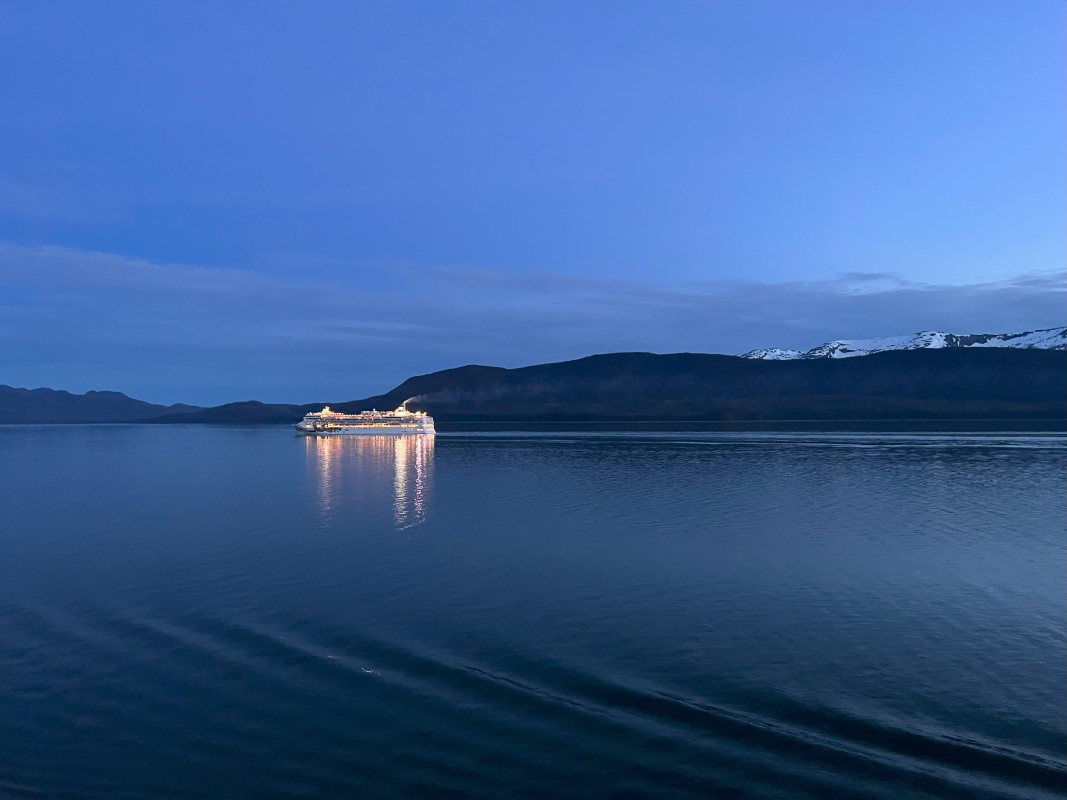 A photo taken at dusk with a lone cruise ship illuminating the ocean waters.